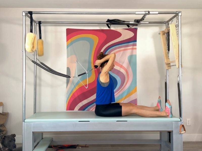 Tư thế chuẩn bị thực hiện động tác Pilates Seated Forward Bend with Neck Stretcher trên Cadillac.