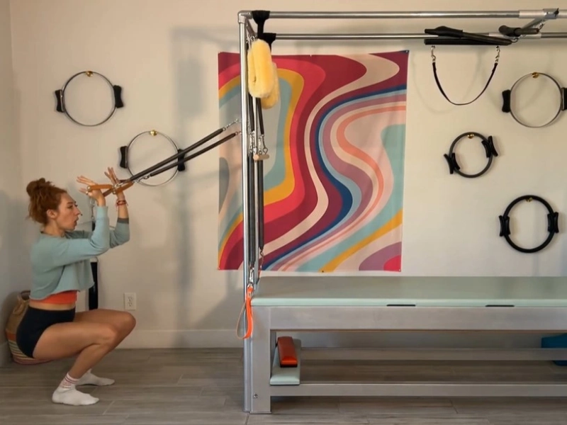 Thực hiện động tác Squats with Standing Arm Springs trên Cadillac
