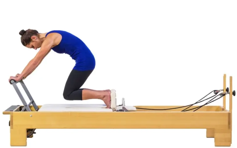 The Pilates Knee Stretches Round Back exercise is performed on a Reformer.