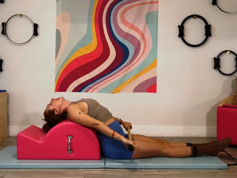 Perform the Pilates Reach Back with Bar on Spine Corrector.